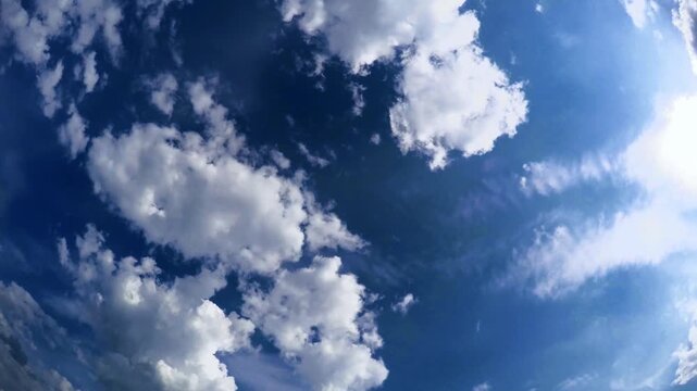 Ultrawide angle time lapse video of fluffy white cumulus clouds fast moving across a vibrant deep blue sky on a clear sunny day. Perfect dynamic natural background for environment, weather, and motion