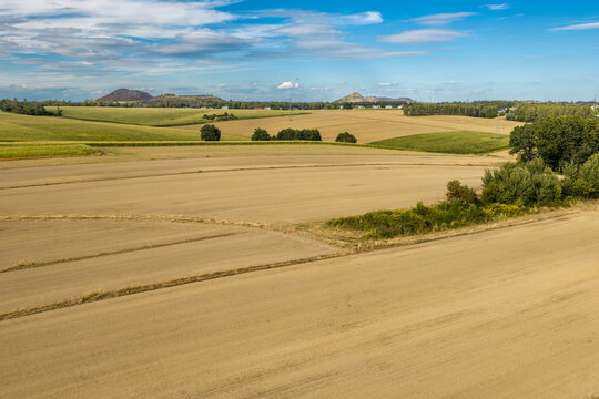 Agricultural landscape with harvested fields and distant slag heaps under blue sky
