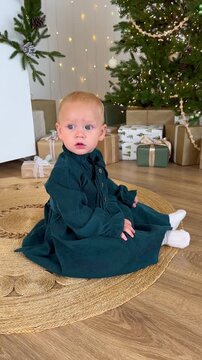 Baby sits beside a decorated Christmas tree and wrapped gifts. A toddler celebrates the holiday season at home.
