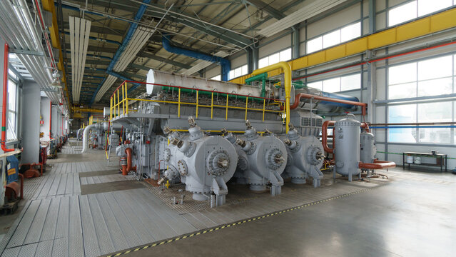 View of a large industrial gas compressor engine inside a factory facility with complex piping and metal flooring in Latvia.