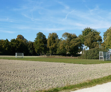 View of a rural soccer field for kids situated among cultivated farm meadows and lush trees under a clear blue sky in Garching, Bavaria, Germany.