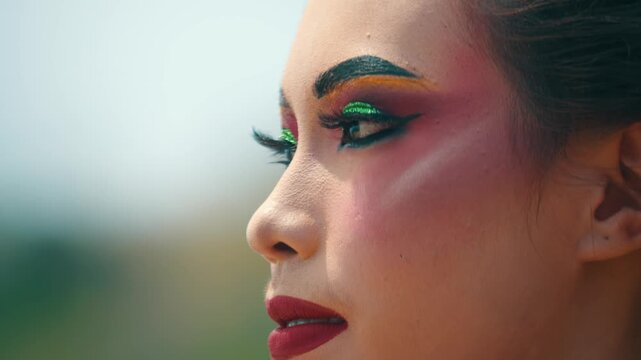 Extreme close-up showing the texture of skin and heavy makeup on an Indonesian dancer's eye, staring intently ahead against a blurred background.
