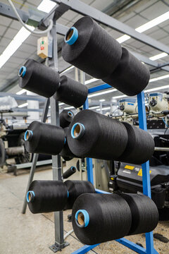 View of black yarn spools arranged on a blue metal rack in a denim factory production line in Karachi, Sindh, Pakistan.