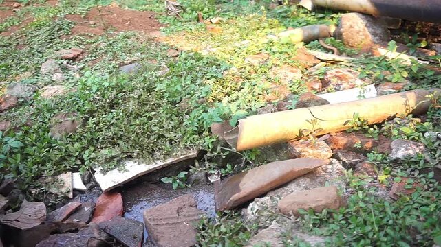 Leaking old pipe discharging dirty water onto muddy ground surrounded by green vegetation and debris.