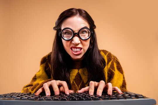 Frustrated woman typing on keyboard with oversized glasses and intense expression in vintage sweater, humorous nerdy programmer or writer at computer