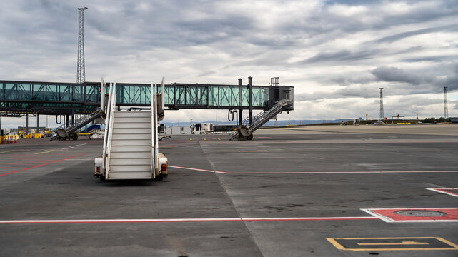 View of a mobile passenger boarding stair on the airport tarmac with jet bridges and a cloudy sky in Iceland.