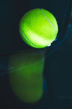 Neon tennis ball on a dark glossy surface.