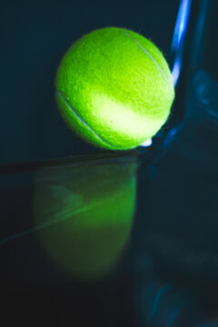 Neon tennis ball on a dark glossy surface.
