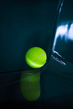 Neon tennis ball on a dark glossy surface.