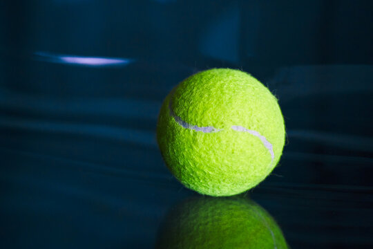 Neon tennis ball on a dark glossy surface.
