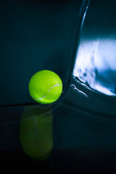 Neon tennis ball on a dark glossy surface.
