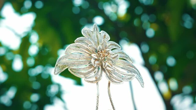 A beautiful silver Kembang Goyang or shaking flower hair pin, a traditional accessory for Indonesian brides, displayed against a natural green backdrop.