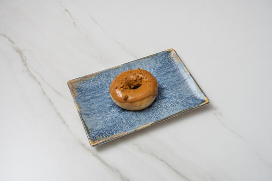 Caramel-glazed mini donut sprinkled with speculoos cookie crumbs on an angled rectangular blue ceramic plate over white marble