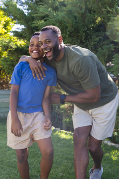 Father and teenage son leaning on grassy lawn, laughing, wearing t-shirts, khaki shorts, wristwatch