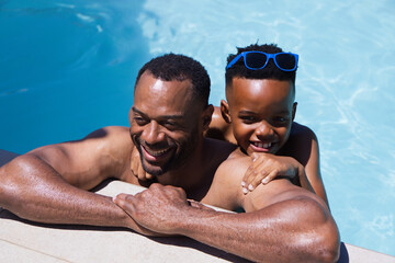Obraz premium Father and child smiling and playing by pool, shirtless father holding son wearing sunglasses