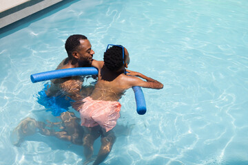 Obraz premium African American dad and daughter in swimwear playing in blue pool holding daughter on foam noodle