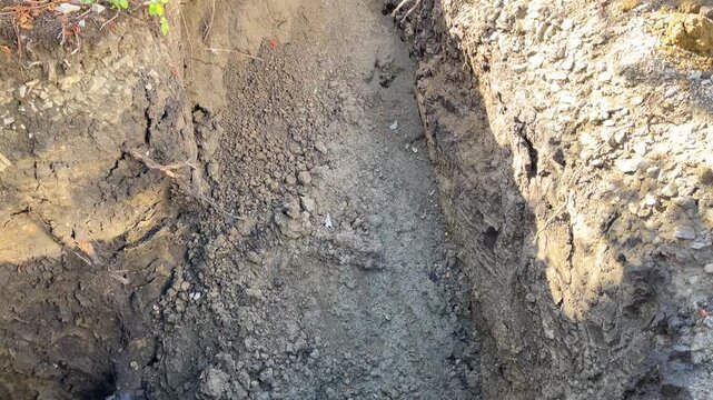 Deep hole dug for gas pipe underground laying. Murky water has collected at bottom around insulated pipe. Walls show marks from excavator bucket