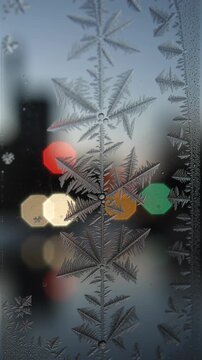 Intricate frost crystals cover a window as colorful city bokeh blurs behind, creating a wintry seasonal background