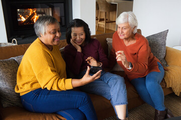 Obraz premium Diverse female friends sitting closely on brown leather couch with lit fireplace