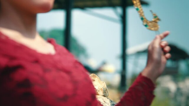 Close-up of a hand gently touching a traditional Javanese golden hair pin displayed on a rock, highlighting the craftsmanship.