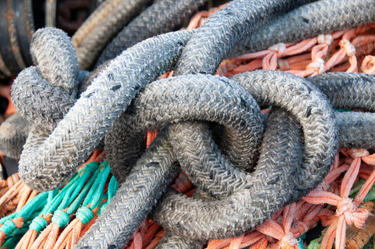 View of weathered nautical ropes knotted together on top of orange and teal fishing nets in Canada.