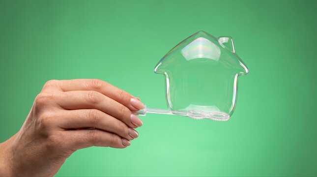 Homeownership vulnerability concept with a hand holding a transparent house soap bubble, expressing property risk and real estate goals