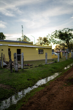 View of a yellow rural house with a wire fence and a small ditch in the foreground, set against a sunset sky in Guaviravi, Corrientes Province, Argentina.