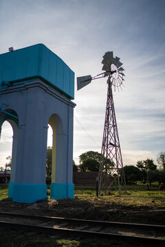 View of a blue water tower and a metal windmill standing in a rural field near railway tracks in Guaviravi, Corrientes Province, Argentina.