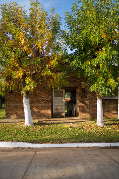 View of a rustic brick building with an open doorway, framed by two trees with white-painted trunks, situated in Guaviravi, Corrientes Province, Argentina.