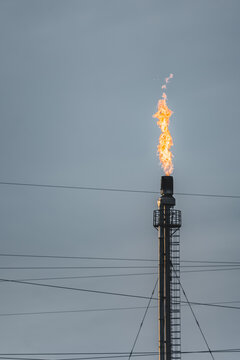 Oil refinery with tall flare stacks and chimneys in the Kazakh steppe; industrial facility at sunset with flames burning from the stacks