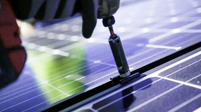 View of a solar installer securing a photovoltaic panel with a power drill in Los Angeles, CA, United States.