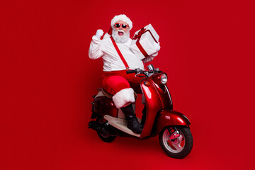 Obraz premium Santa Claus on a red scooter delivering a wrapped gift with festive cheer and sunglasses, energetic holiday concept for Christmas celebration and seasonal delivery
