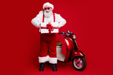 Obraz premium Santa Claus holding a wrapped gift next to red scooter in festive Christmas scene with sunglasses and joyful holiday spirit
