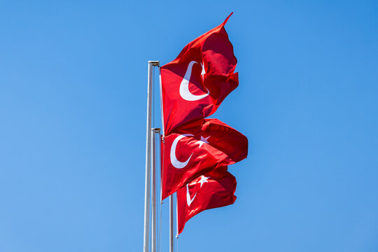 Three red Turkish flags bearing white crescent and star wave on metal poles against a vivid blue sky, evoking national pride, patriotism, unity and cultural identity in an outdoor setting