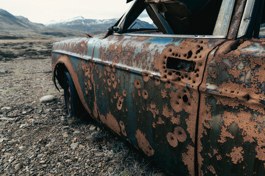 View of a rusted, bullet-riddled vintage car abandoned in the desolate landscape of Stokksnes, Iceland.