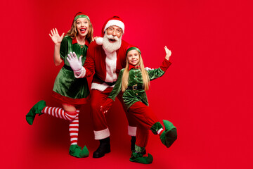 Obraz premium Santa and two cheerful elves posing together in festive Christmas costumes against a bright red background for holiday family fun and seasonal celebration