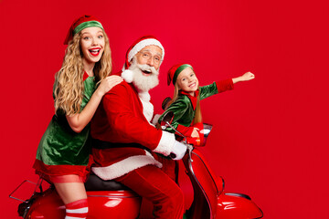Obraz premium Santa and two elves riding a red scooter and laughing together in festive Christmas costumes against a red background