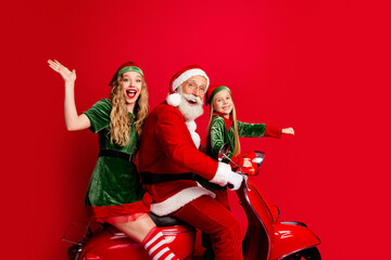 Obraz premium Santa and two cheerful elves riding a red scooter together for a festive family Christmas celebration