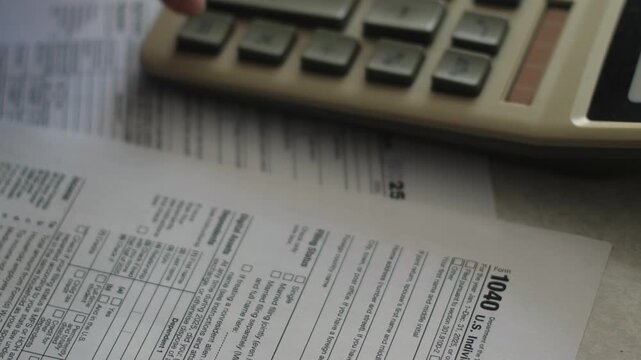 The U.S. Form 1040 tax return document lies on a desk next to an accounting calculator. A clear close-up shot illustrates financial reporting, tax filing, and bookkeeping processes