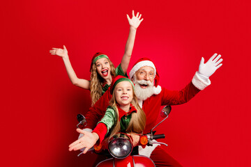Obraz premium Santa with two joyful elves riding a red scooter celebrating Christmas family fun and holiday excitement