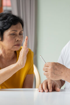 elderly southeast asian wife persuading her 70s husband to stop smoking indoors, concept image for quit smoking or stop smoking