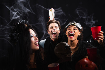 Obraz premium Multicultural friends joyfully celebrate Halloween with drinks at a costume party