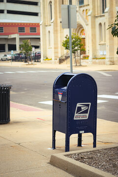 Peoria, IL, US - Aug 29, 2026: A blue United States Postal Service (USPS) outdoor collection mailbox on a sidewalk with church in the background