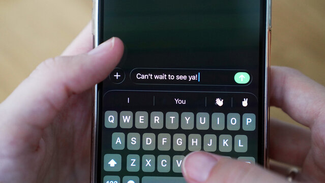 Hands typing a message 'Can't wait to see ya!' on the screen of the smartphone, internet online communication, messaging, connection, keeping in touch