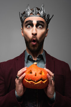 Handsome man dressed as an evil king with Halloween makeup and a pumpkin