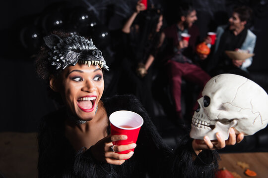 Happy african american woman with wolf mask holding skull while joyfully celebrating Halloween 