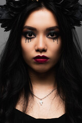 Fototapeta premium Young woman embraces spooky elegance in witch makeup and floral crown