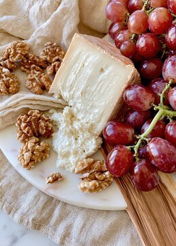 Red grapes with aged cheese and walnuts arranged on linen cloth and wooden serving board