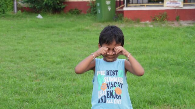 Young child crying outdoors on green grass in blue tank top