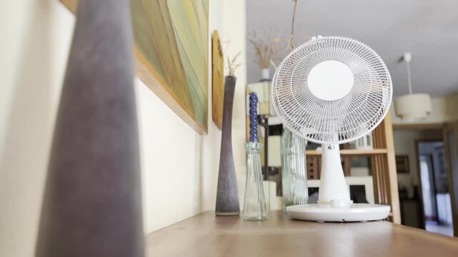 White Table Fan on Wooden Sideboard With Vases in Living Room Interior 